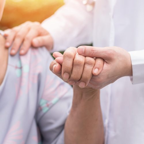 Elderly senior dementia patient (aging old adult person) in nursing hospice home holding geriatrician doctor's hand having happy medical health care from hospital carer or caregiver healthcare service